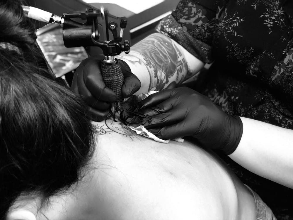 Vivir en Brisbane fotografía en blanco y negro de cómo un tatuador le hace un tatto a una chica con un moño en la espalda